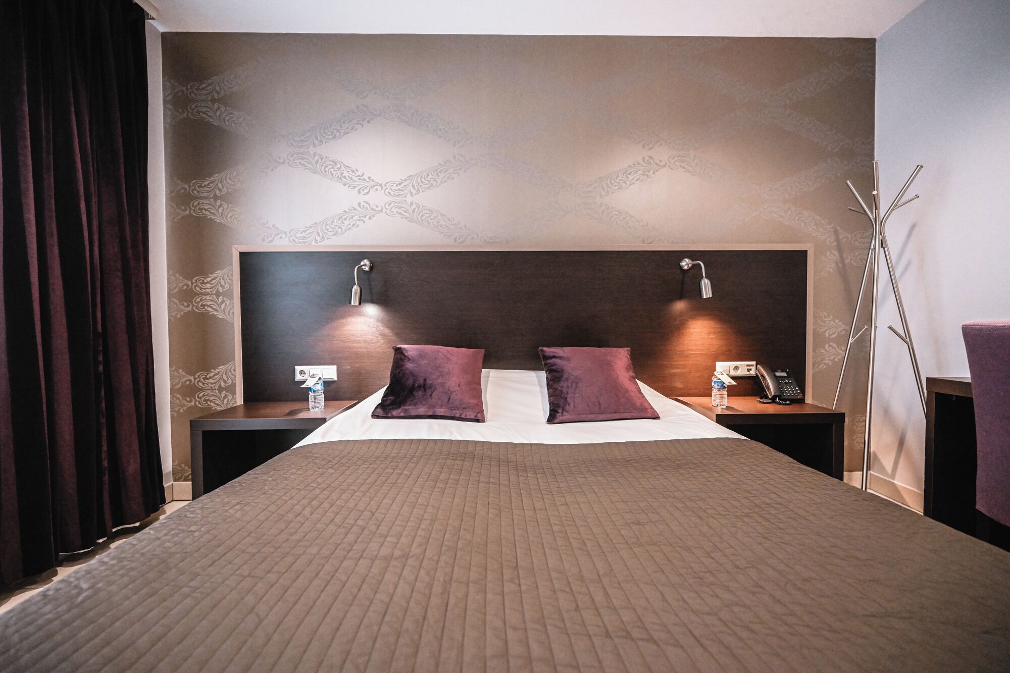 A hotel room with a large bed, two bedside tables, two lamps, and a nightstand with a phone.