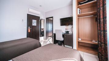 Habitación de hotel con dos camas, un escritorio con silla, armario, televisor y baño visible a través de una puerta abierta.
