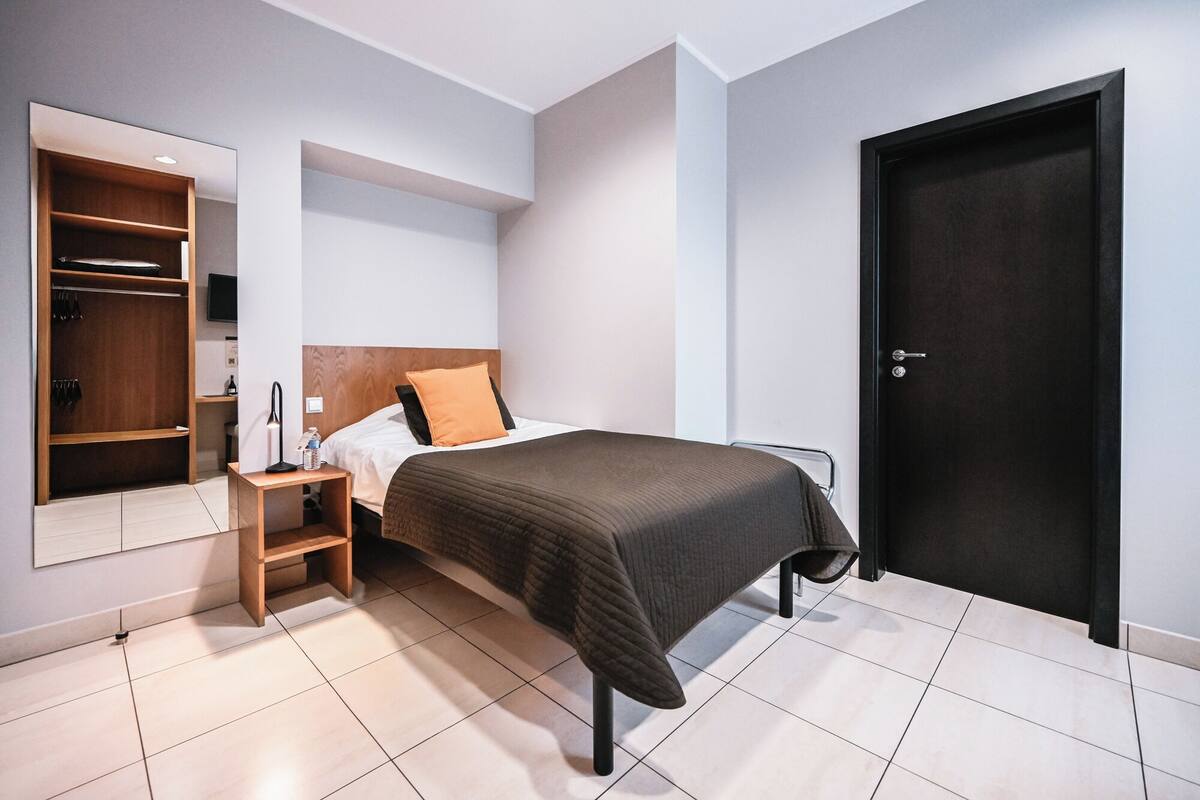 A bedroom with a bed, a wardrobe, a bedside table, and a door.