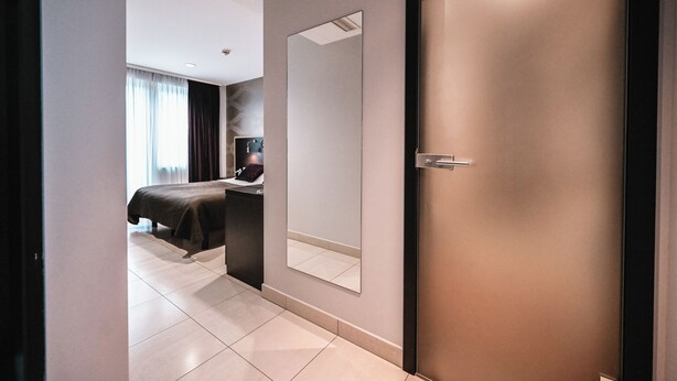 Una habitación de hotel moderna con una cama grande, un escritorio con silla, un espejo y una puerta.