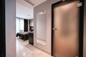 A modern hotel room with a large bed, a desk with a chair, a mirror, and a door.