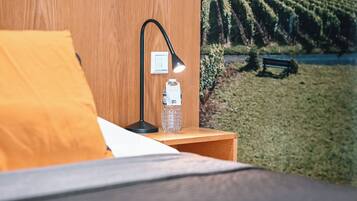 A neatly made bed with a yellow pillow, a black desk lamp, and a water bottle on a wooden nightstand.