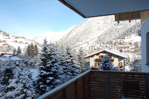 A snowy mountain village with traditional houses, a wooden balcony, and a clear view of the surrounding mountains.
