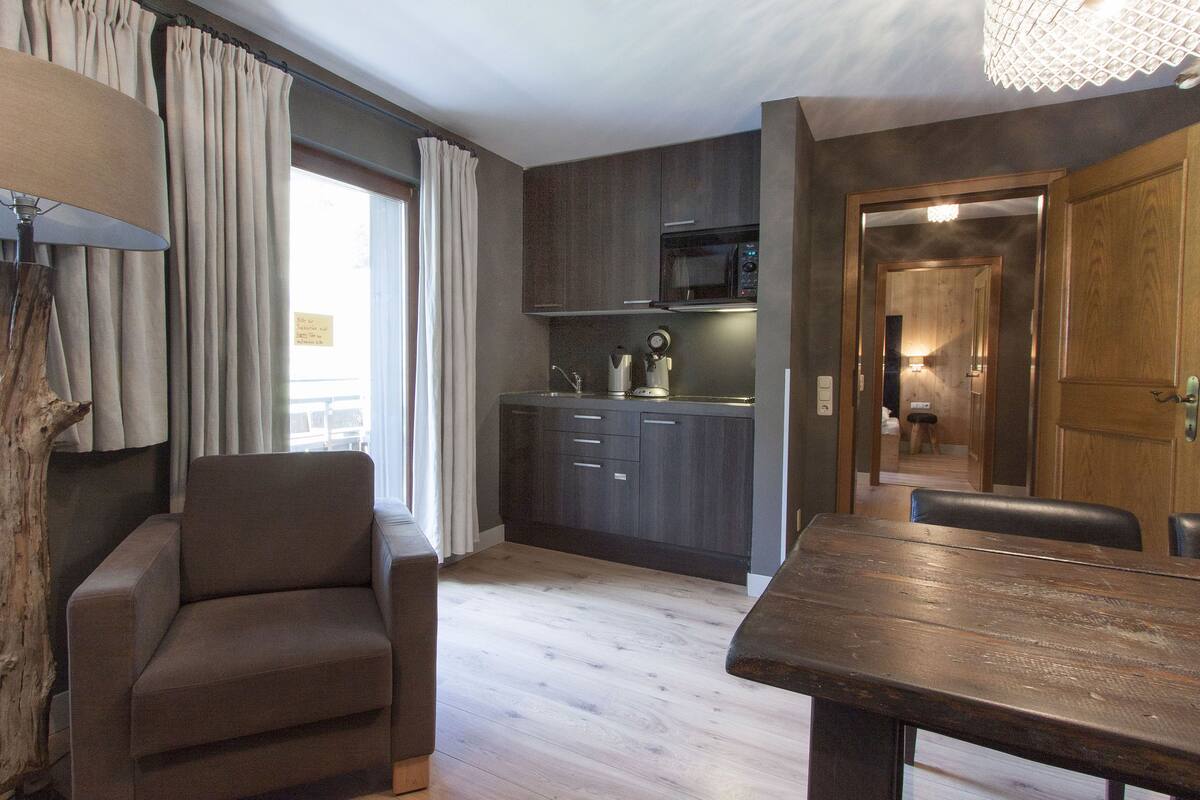 A modern kitchen with dark cabinets, a microwave, and a coffee maker. There is a dining area with a wooden table and chairs.