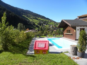 A swimming pool with a red playhouse, a wooden building, and a view of a green valley with houses.