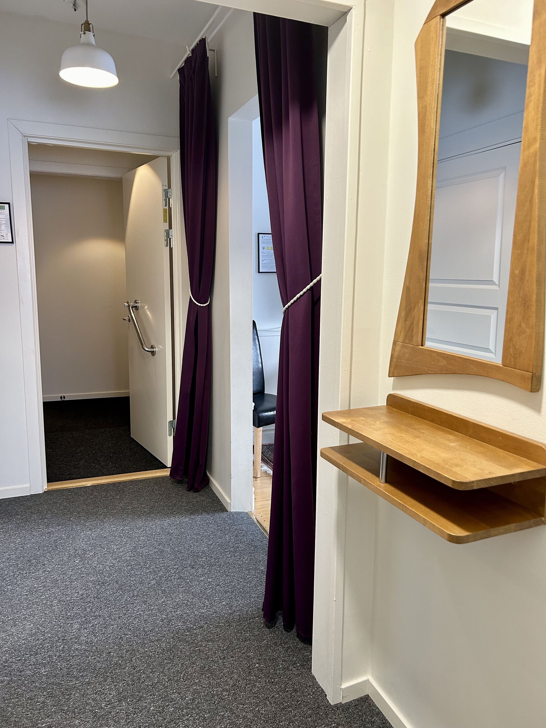 A hallway with a wooden bench, a door with a handrail, and purple curtains.