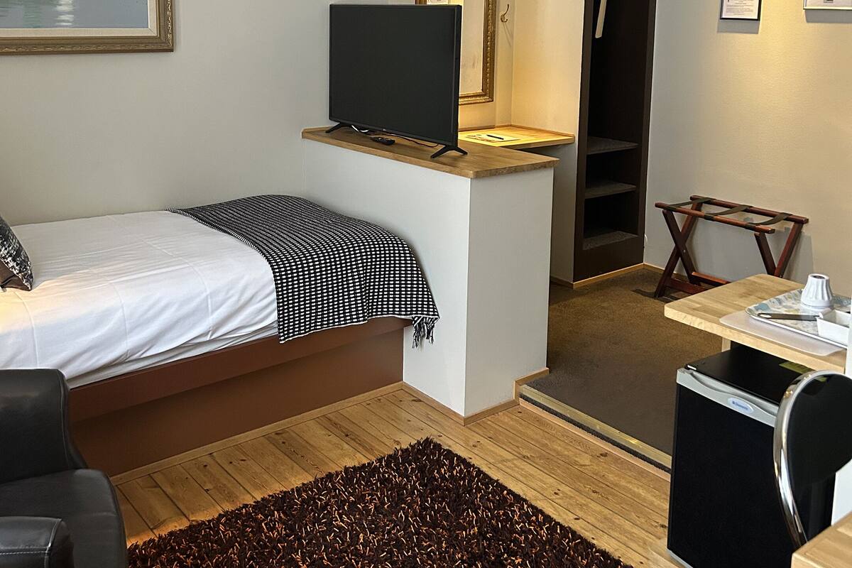 A compact hotel room with a bed, a desk, a television, a chandelier, and a mirror.