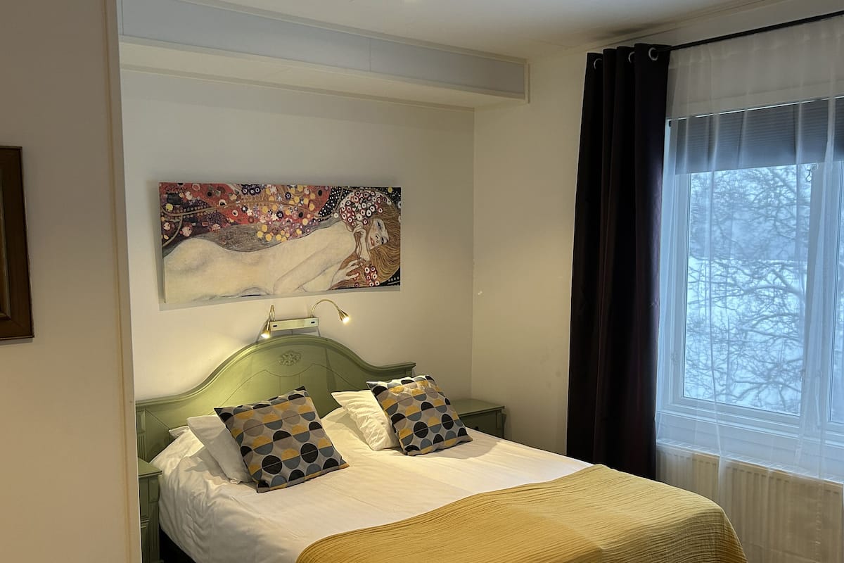 A neatly made bed with patterned pillows, a green headboard, and a painting above it.