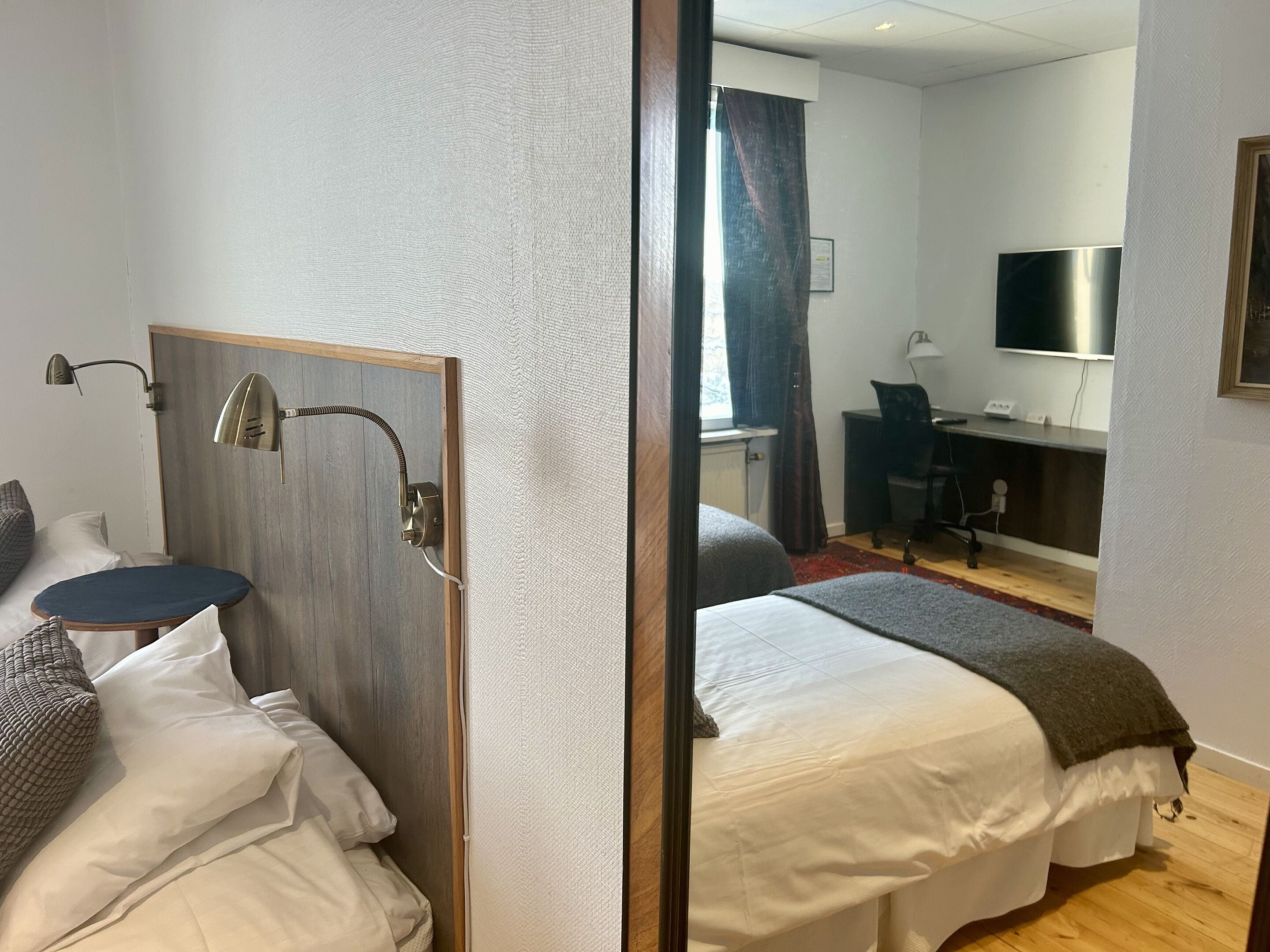 A hotel room with a bed, a desk, a chair, a TV, and a window with curtains.