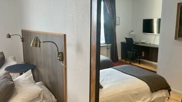 A hotel room with a bed, a desk, a chair, a TV, and a window with curtains.