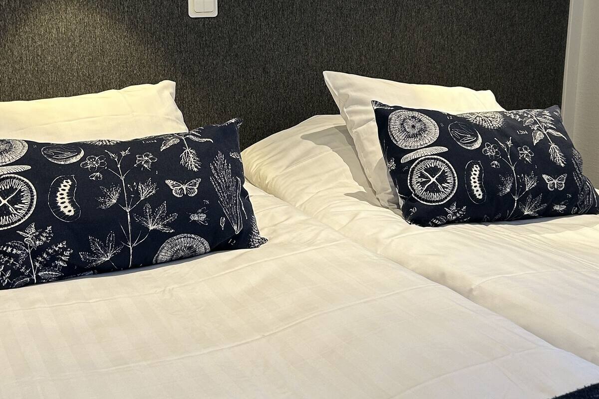 A neatly made bed with white linens and two decorative pillows with a nature-themed pattern.