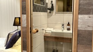 Une salle de bain avec une porte en bois, un lavabo surmonté d’un miroir et un espace douche.