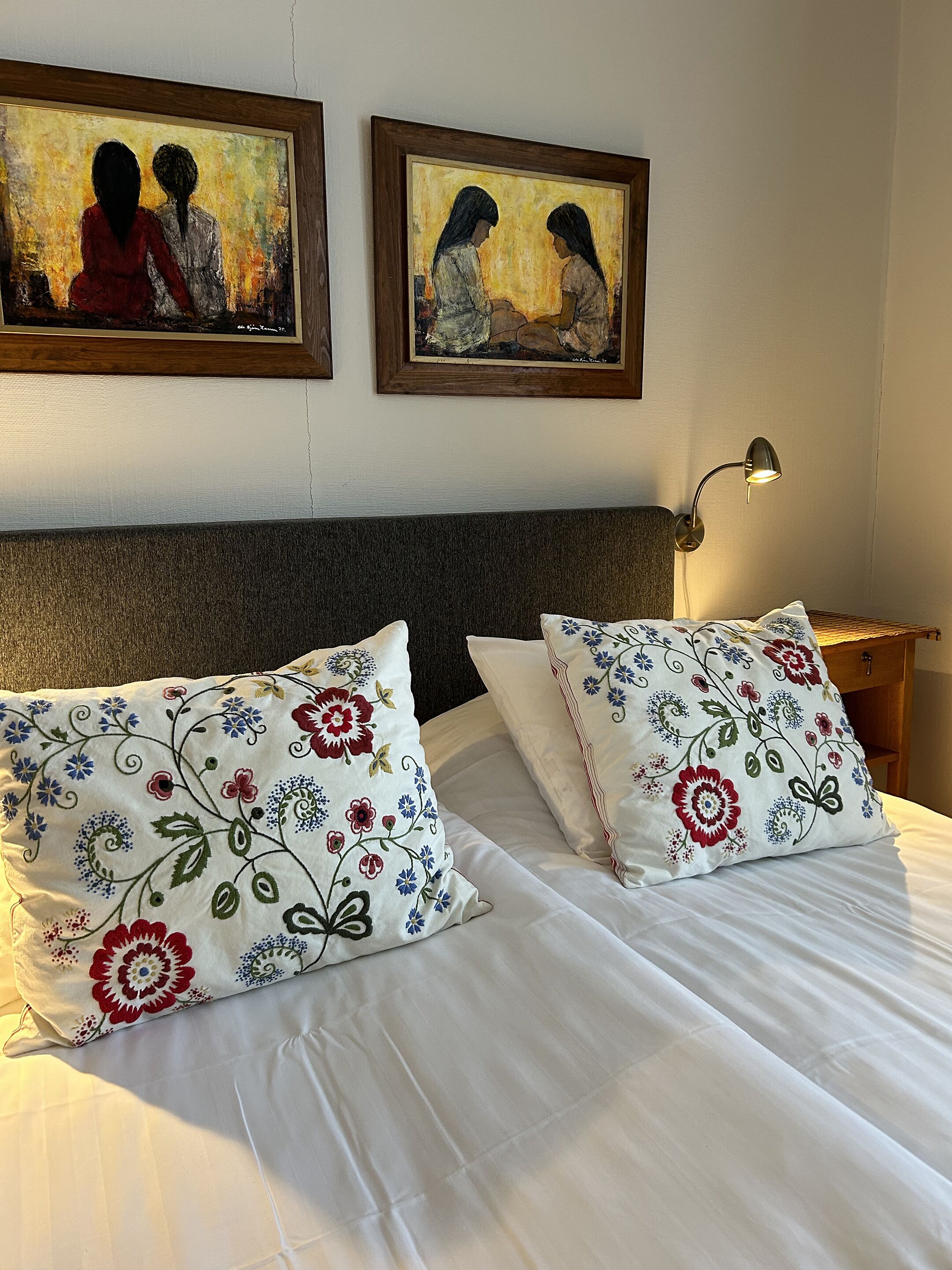 Una cama bien hecha con almohadas estampadas y dos cuadros en la pared de arriba.
