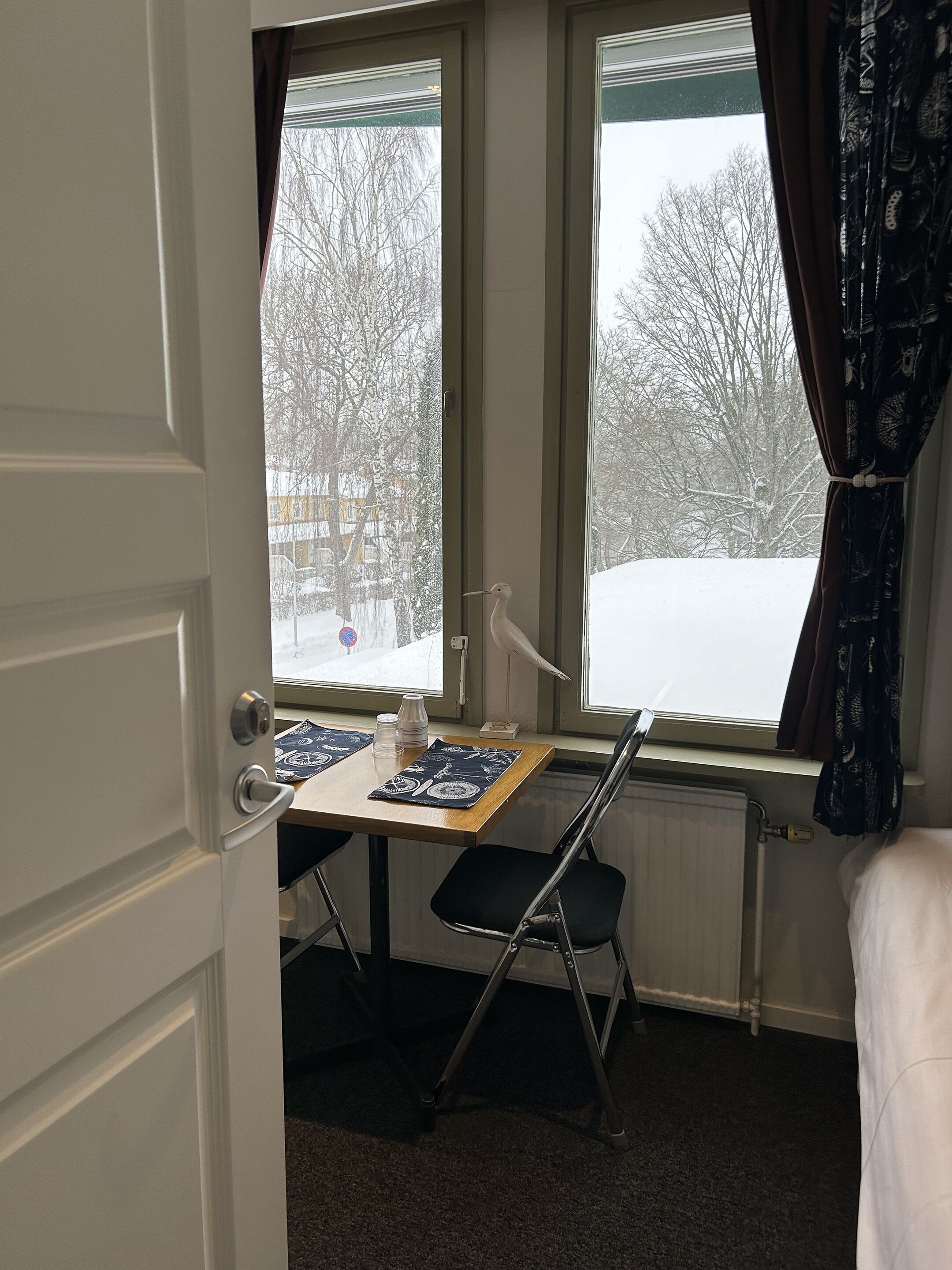 Ett rum med ett fönster, ett element, ett bord med en stol och en säng.