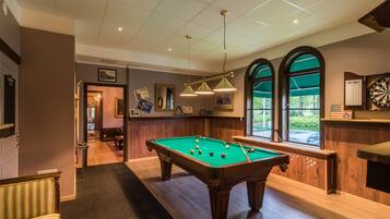 A pool table in a room with wooden walls and a dartboard.