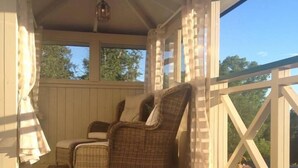 Une véranda avec deux fauteuils en osier, une petite table et un banc.