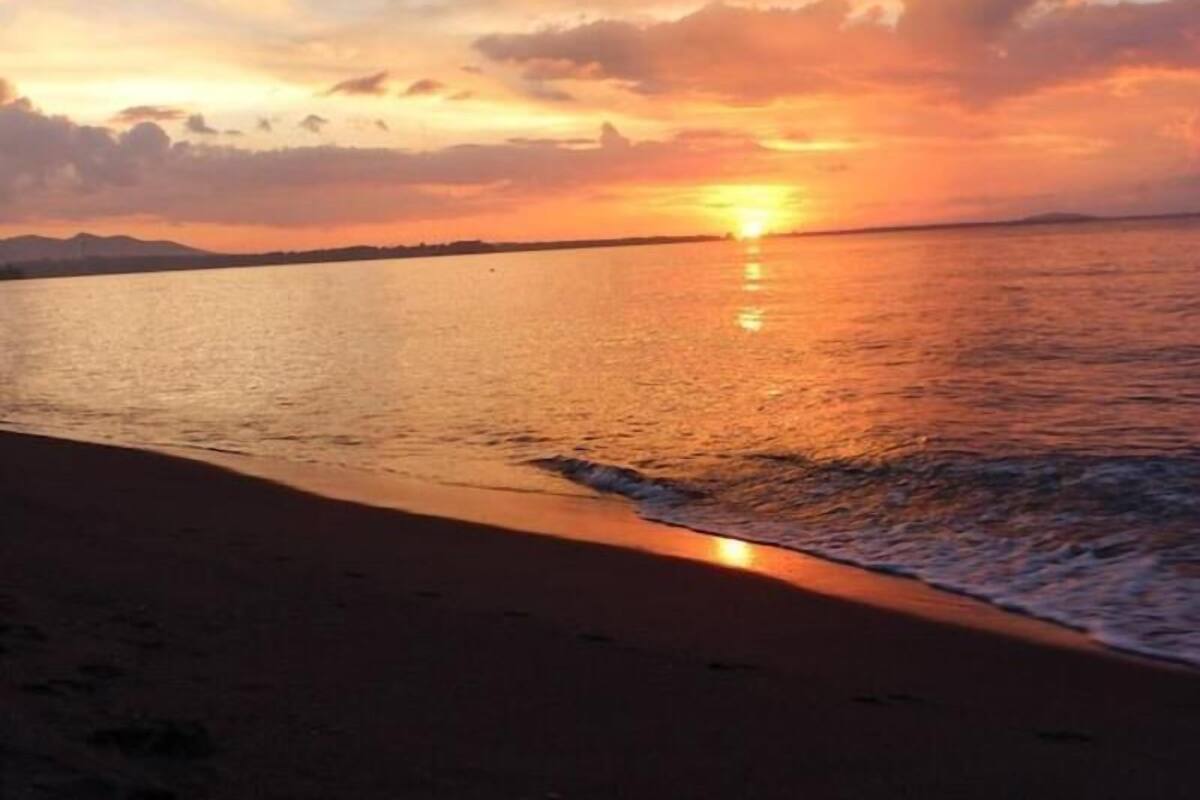Un atardecer sobre una playa con aguas tranquilas y un horizonte despejado.