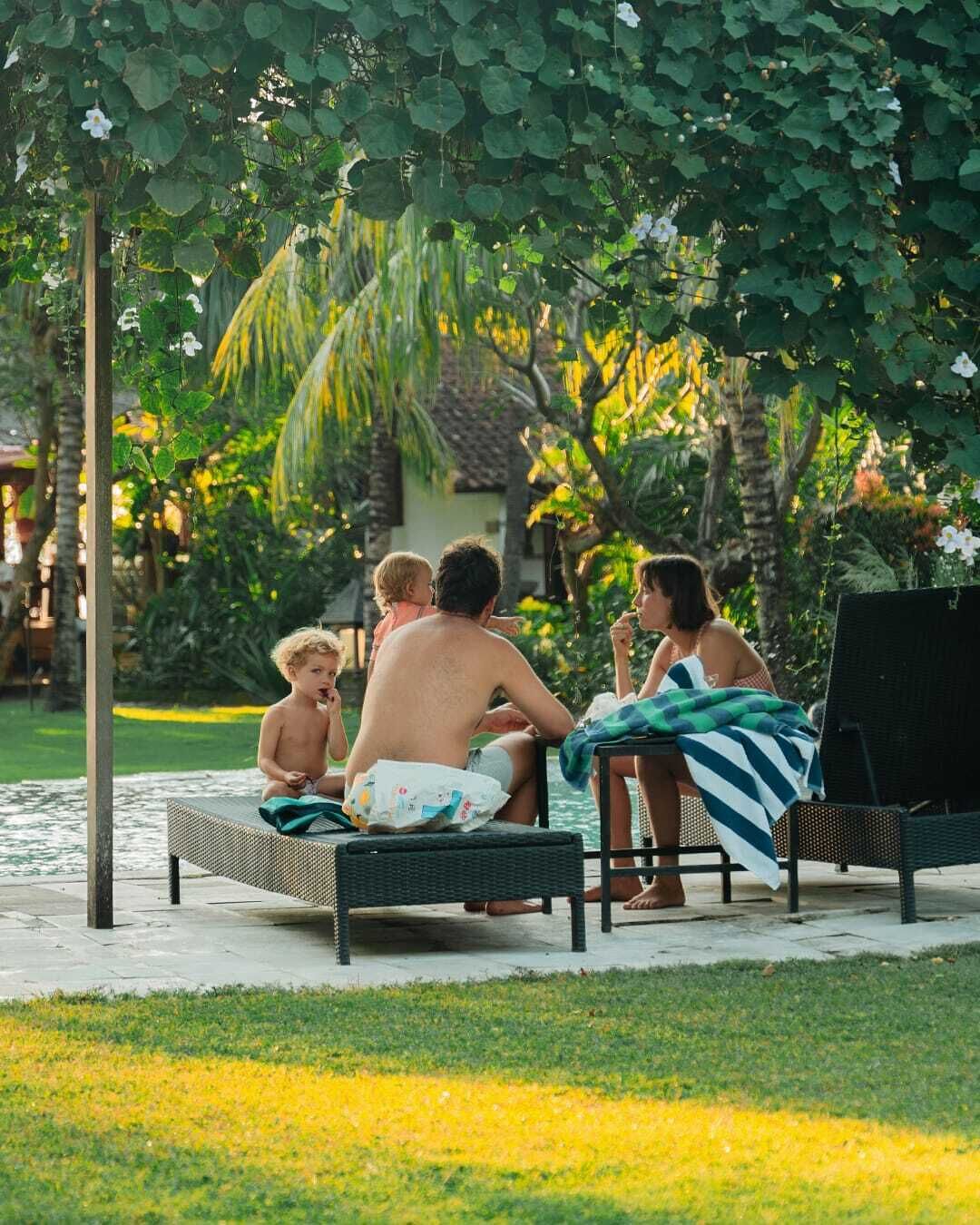 A poolside area with lounge chairs and a small table, surrounded by lush greenery and a palm tree.