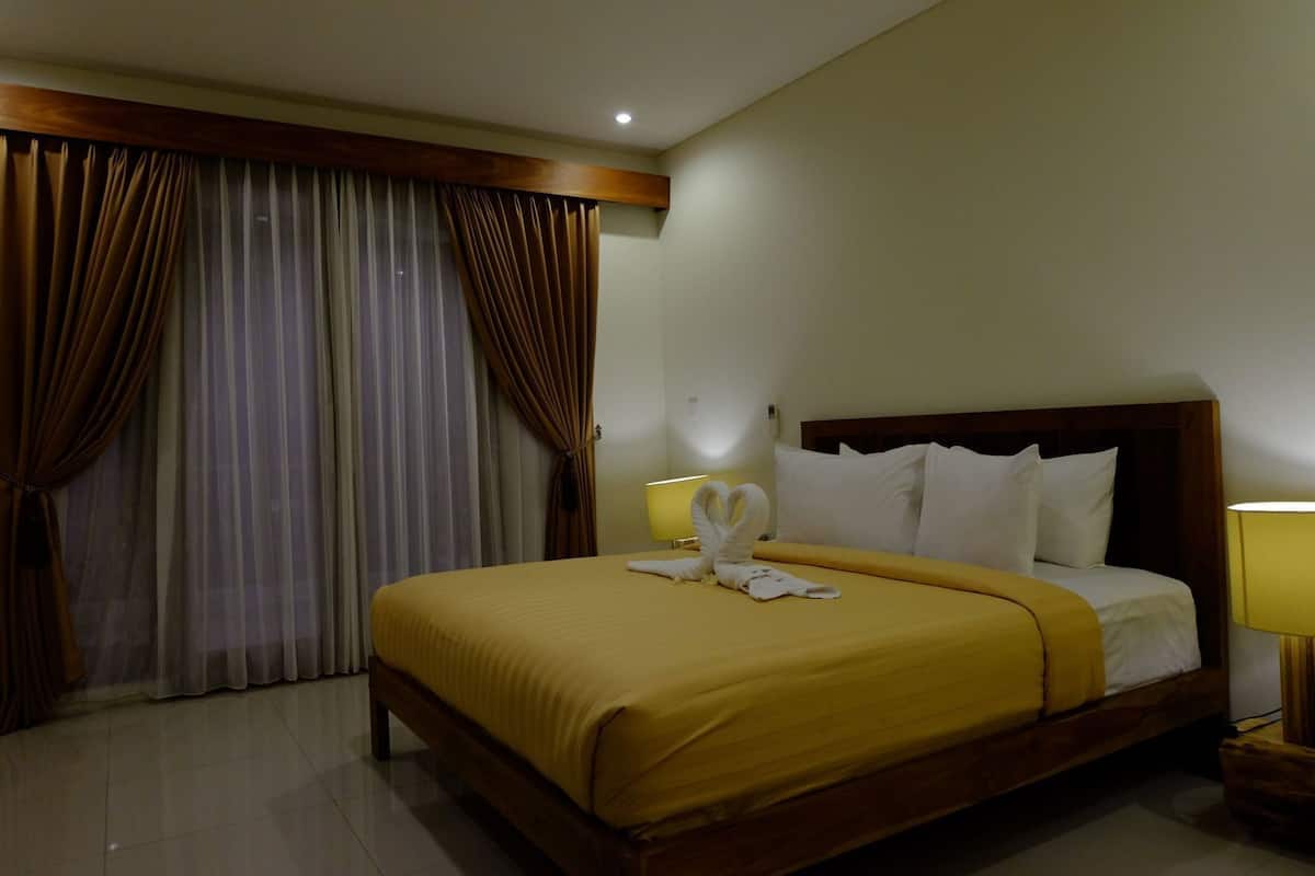 Une chambre d’hôtel avec un grand lit, des rideaux, une lampe de chevet et un luminaire fixé au mur.