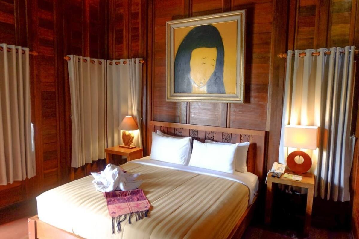 Une chambre d’hôtel avec un mur lambrissé en bois, un lit avec du linge de lit blanc, une table de chevet avec une lampe et une œuvre d’art encadrée au-dessus du lit.