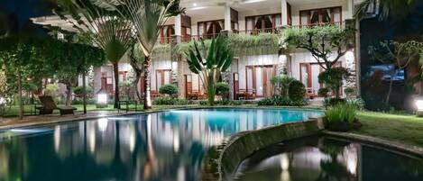 A hotel with a swimming pool, lush greenery, and a well-lit exterior.
