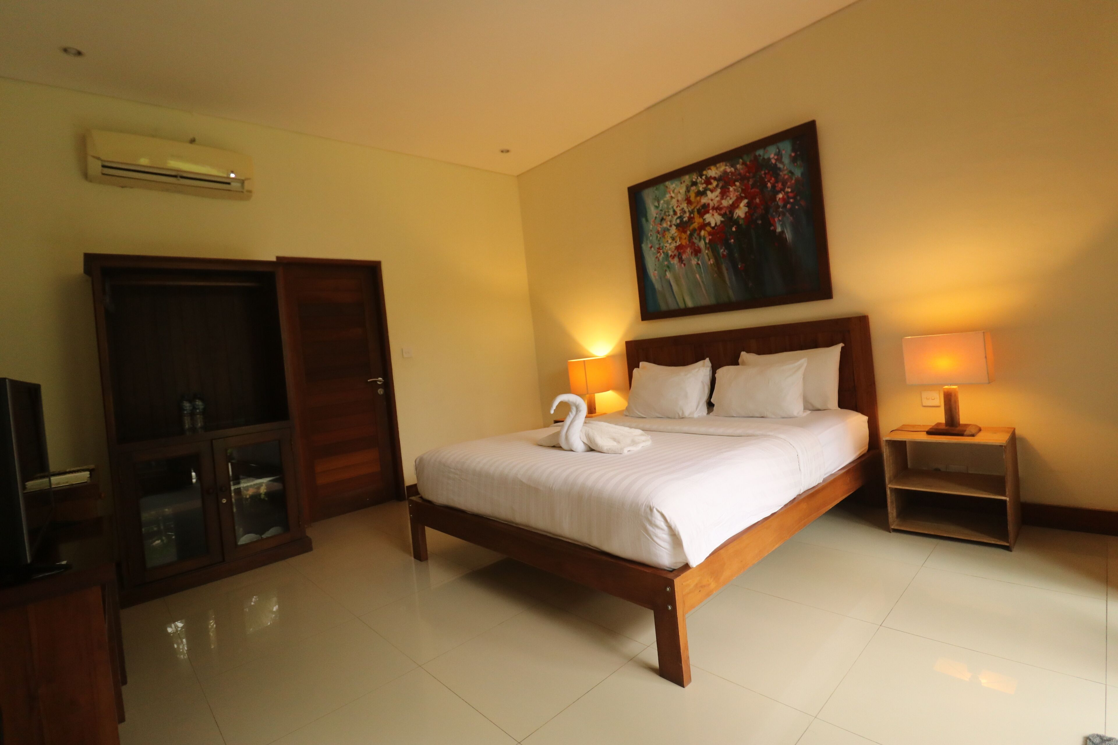 Quarto de hotel com cama de madeira, televisão, guarda-roupa e um quadro na parede.