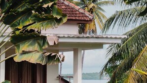 A house with a balcony overlooking a body of water, surrounded by tropical vegetation. - Mina Tanjung Hotel (Tanjung)