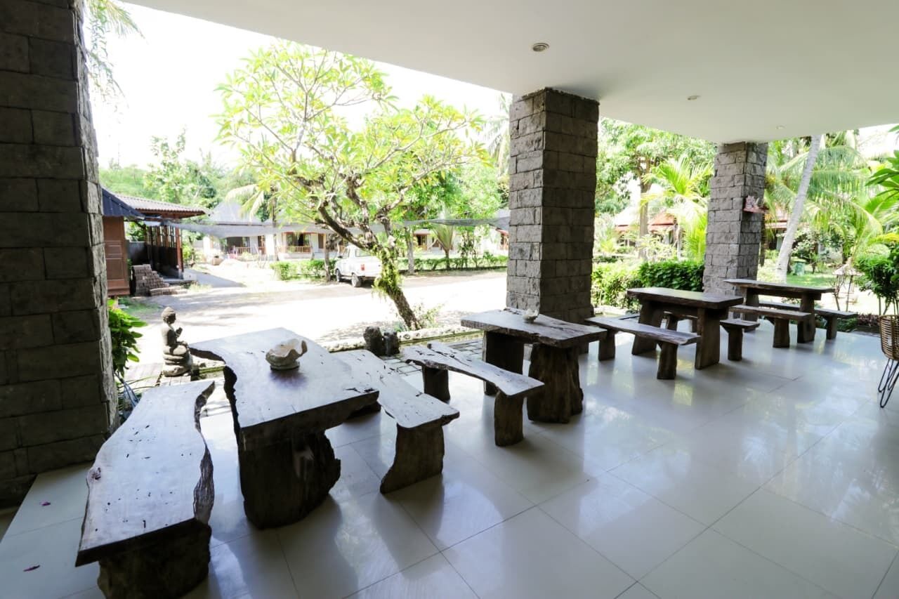 An outdoor patio area with stone tables and benches, surrounded by greenery and a view of a street.