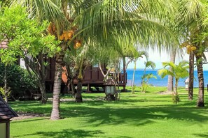 Un jardín tropical con una estructura de madera, palmeras y vistas al mar.