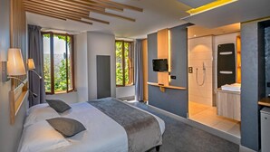A modern hotel room with a large bed, a TV, a shower area, and a view of greenery outside. - Gilles Moreau (Laguiole)