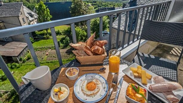 A breakfast setup on a balcony with a scenic view, including bread, eggs, fruit, and a glass of orange juice. - Gilles Moreau (Laguiole)