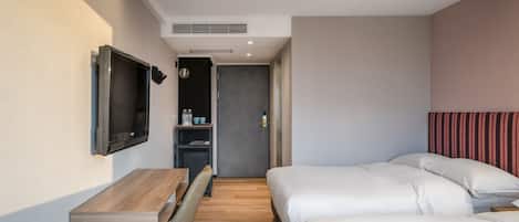 Una habitación de hotel moderna con un escritorio de madera, un televisor de pantalla plana, dos camas y una kitchenette pequeña.