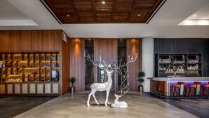 Un vestíbulo con techo de madera, una recepción, una zona de bar y una escultura decorativa de un ciervo.