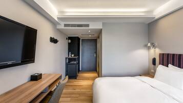 A modern hotel room with a flat-screen TV, a wooden desk, a bed with white linens, and a small seating area.