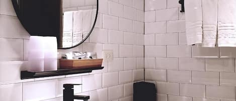 Un baño con azulejos blancos, un lavabo negro, un espejo y un perchero para toallas.