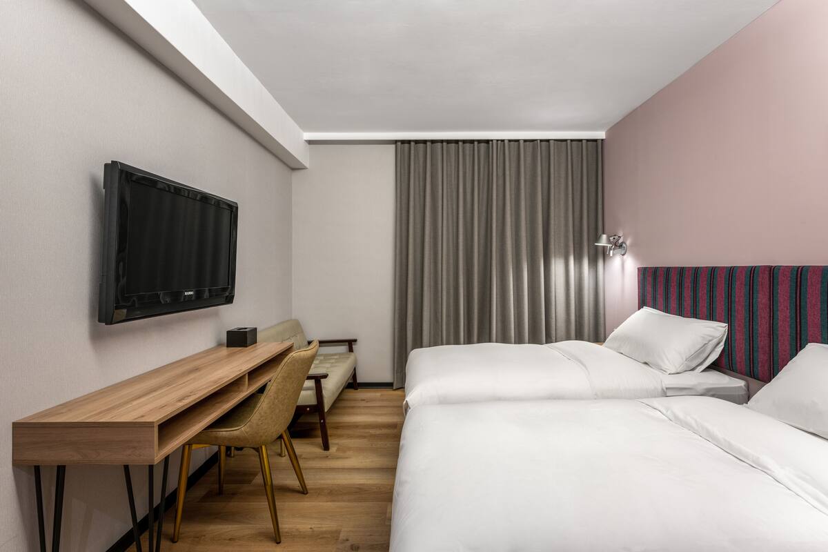 A hotel room with a bed, a desk, a chair, a television, and a window with curtains.