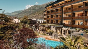 A hotel with multiple balconies, a swimming pool, and a mountainous backdrop. - Dolce Vita Hotel Jagdhof (Laces)