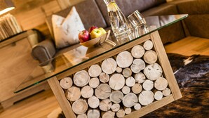 A glass-top table with a wooden frame filled with logs, a bowl of fruit, and two glasses. - Dolce Vita Hotel Jagdhof (Laces)