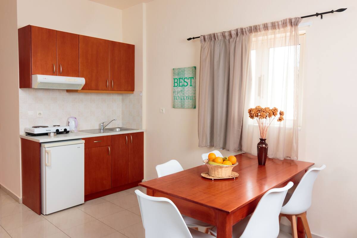 Una cocina compacta con armarios de madera, un refrigerador blanco y una mesa de comedor con sillas blancas.