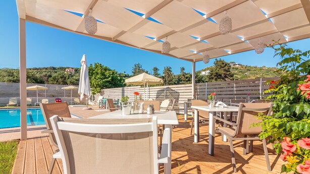 An outdoor patio with tables and chairs, a pool, and a pergola with hanging lights.