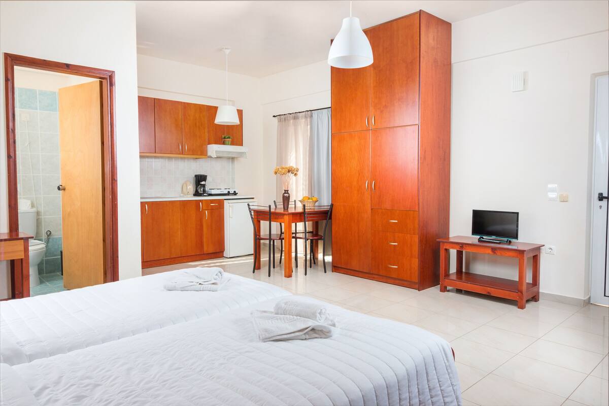 Una habitación de hotel con una cama grande, un armario de madera, una pequeña zona de cocina y un televisor sobre un mueble de madera.