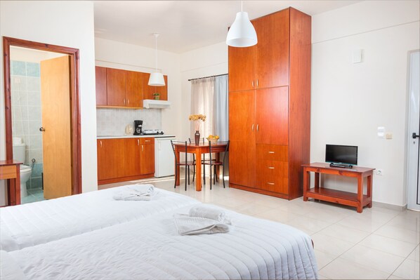 Una habitación de hotel con una cama grande, un armario de madera, una pequeña zona de cocina y un televisor sobre un mueble de madera.