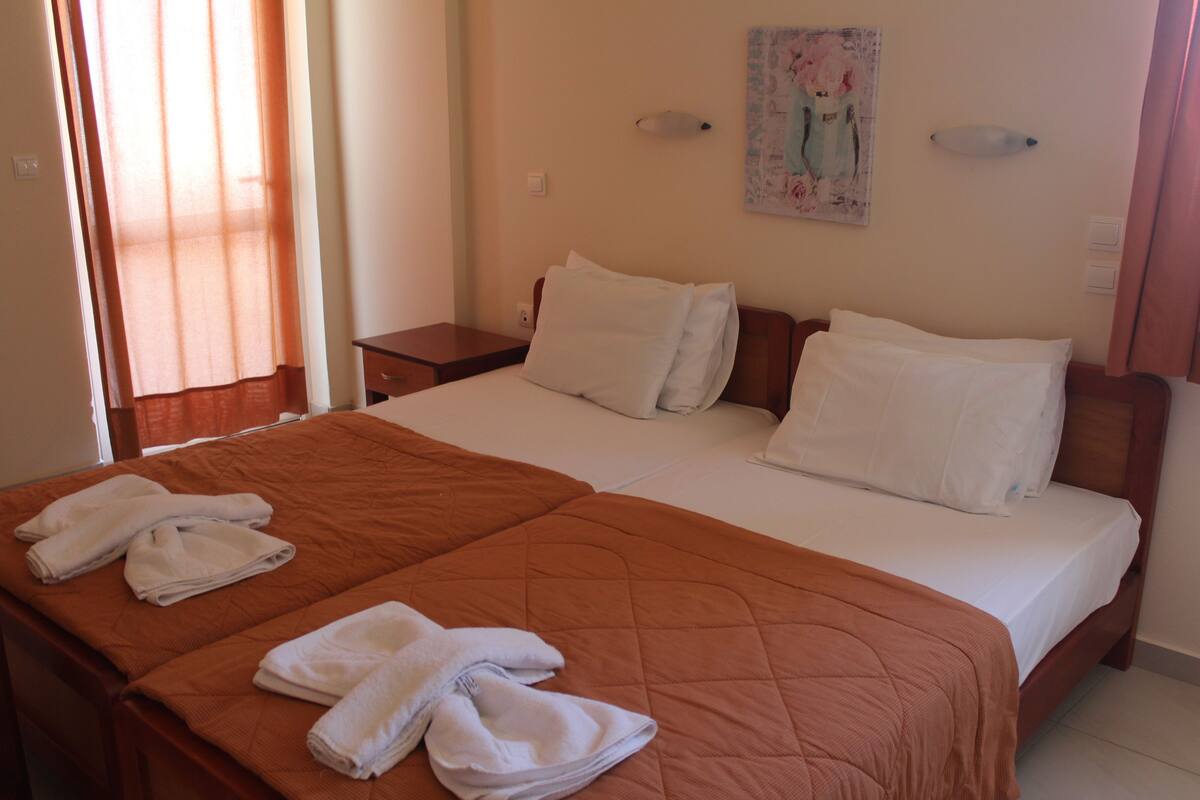 Habitación de hotel con una cama grande, dos mesitas de noche y una ventana con cortinas.