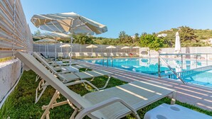 A poolside area with lounge chairs and umbrellas, a clear blue pool, and a view of a hillside with buildings.