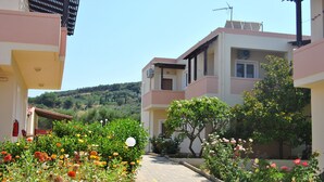 A residential building with a paved pathway, surrounded by lush greenery and flowering plants.