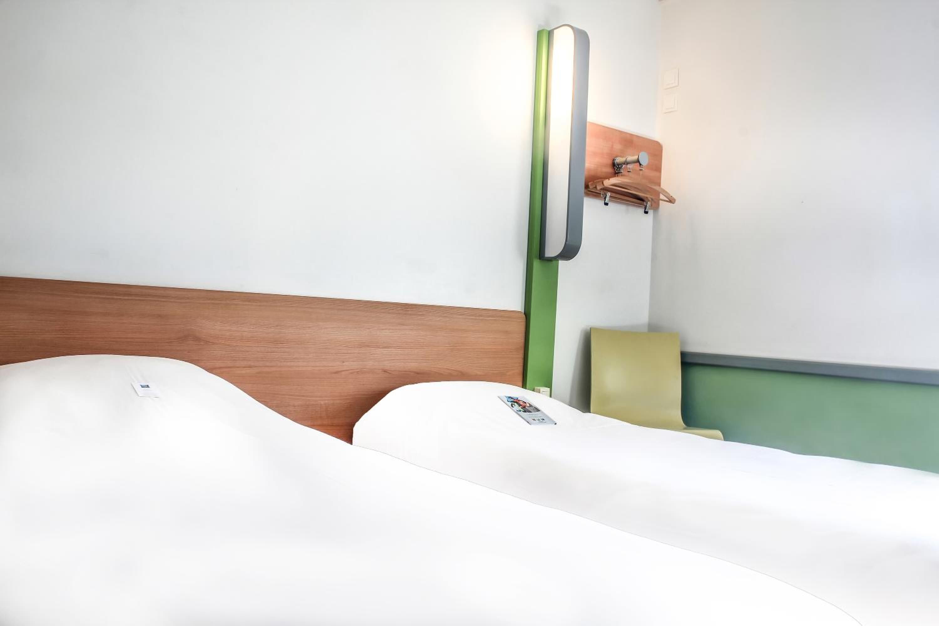 A hotel room with a wooden headboard, a green wall-mounted light fixture, and a single bed with white bedding.
