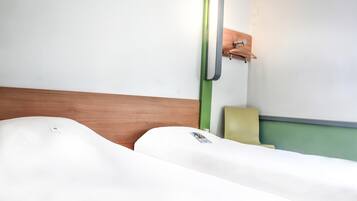 A hotel room with a wooden headboard, a green wall-mounted light fixture, and a single bed with white bedding.