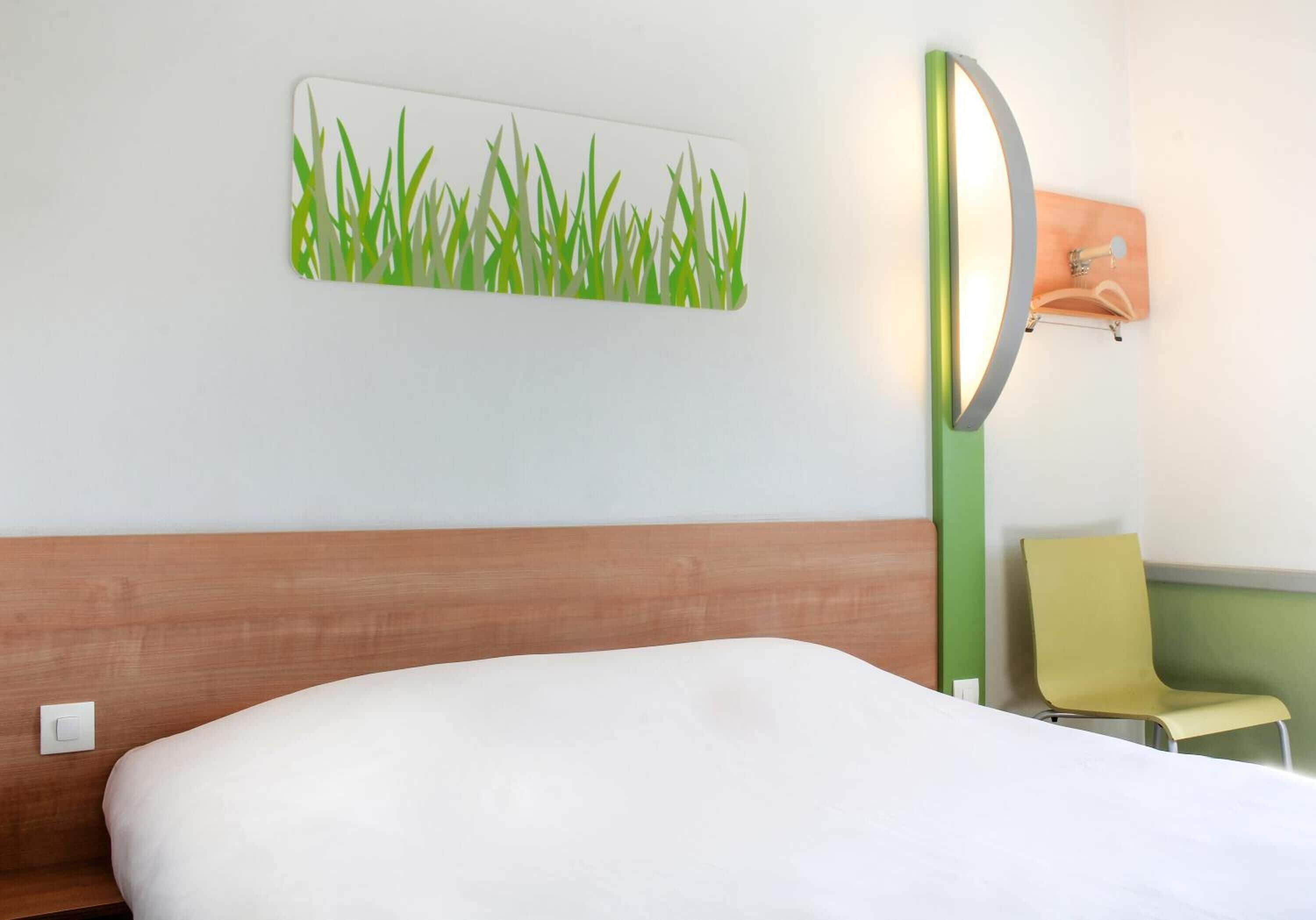 Habitació d'hotel amb un llit, una làmpada penjada a la paret, una cadira i una obra d'art a la paret.