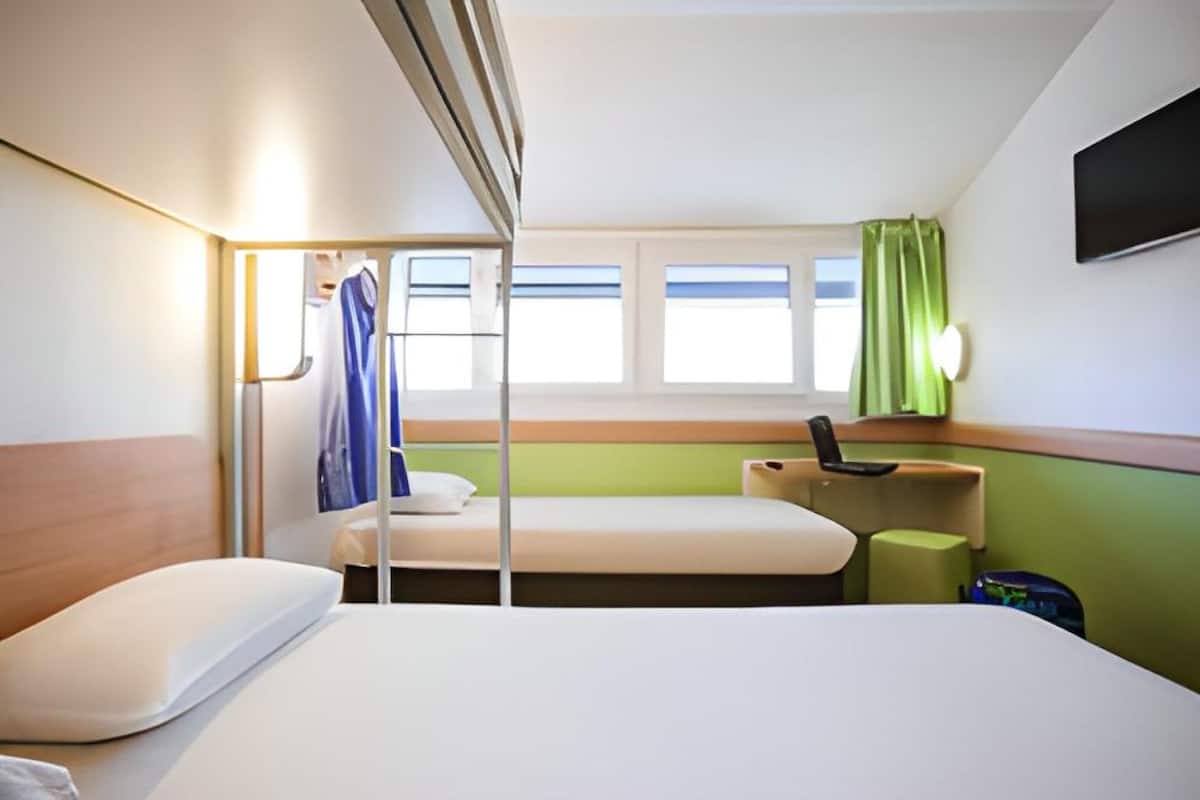 A hotel room with two beds, a desk, a chair, a TV, and a window with curtains.