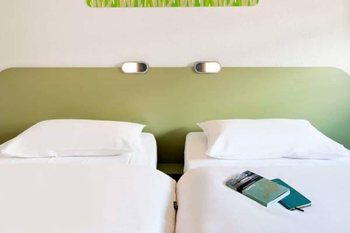 A hotel room with two beds, each with white bedding and pillows. There is a green wall with a grass pattern above the beds.